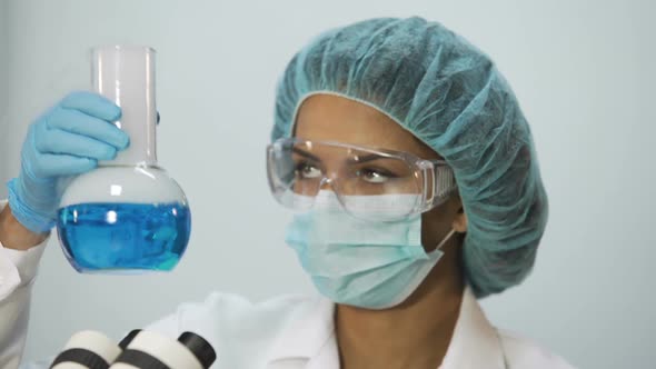 Intern Taking Sample of Blue Liquid and Checking It on Microscope, Laboratory