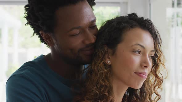 Profiles of happy biracial couple embracing, standing at window and looking into distance