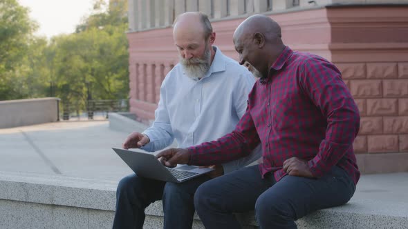 Two Funny Elderly Men Sitting Outdoors Using Laptop Finding Bug Getting Negative News
