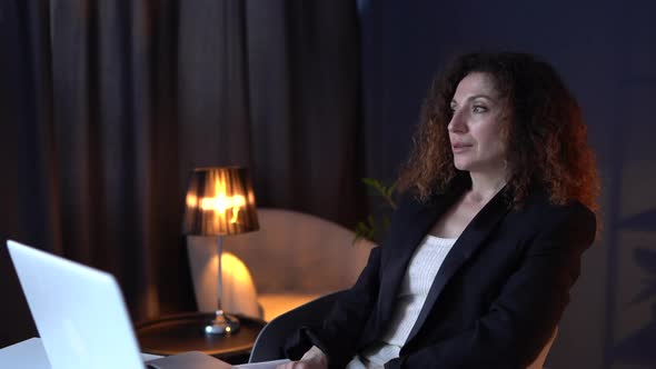 Mature Businesswoman Working on Laptop Holding Coffee Cup at Night in Office