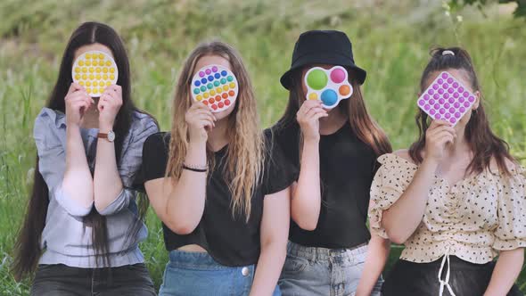 Girls Cover Their Faces with a Toy Pop It While Sitting in the Park