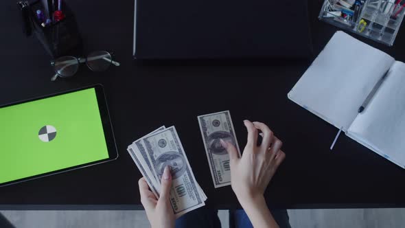 Business Woman Hand Counts Stack of Dollars on Table on Which There is Digital Tablet with Chromakey
