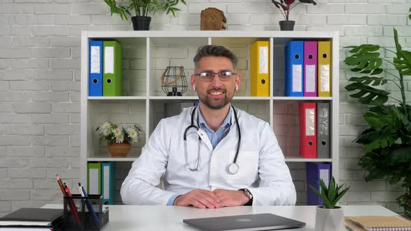 Smiling doctor looks camera listens patient on online video conference call chat