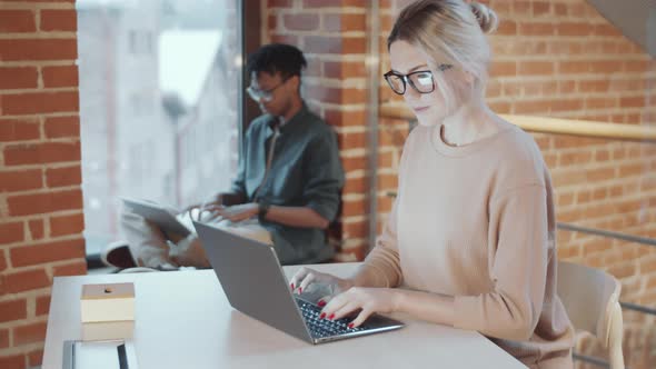 Positive Blonde Woman Using Laptop and Posing for Camera at Office Workplace