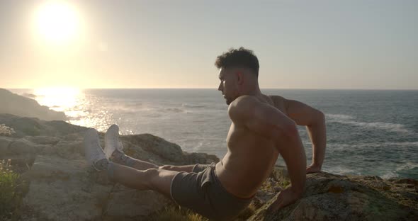 Man with naked torso doing triceps exercises on rocky shore