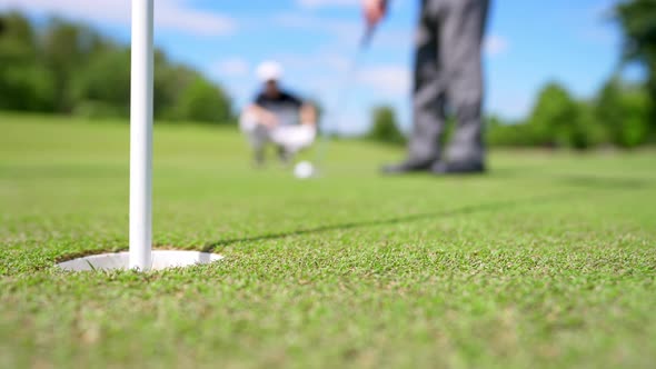 4K Elderly man golfer putting golf ball passing a hole on fairway