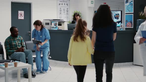 Mother and Little Girl Writing Checkup Report at Hospital Reception Desk