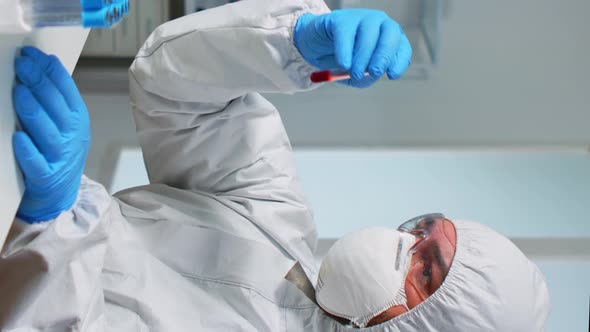 Vertical Video Scientist in Sterile Chemistry Suit Analysing Blood Sample From Test Tub