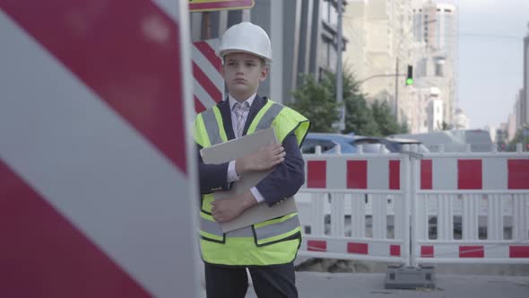 The Little Boy in Helmet, Hard Hat and Uniform Holding Building Plan, Controlling Work