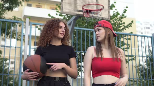 Two Young Sports Women Teenagers with a Basketball Ball Outdoors