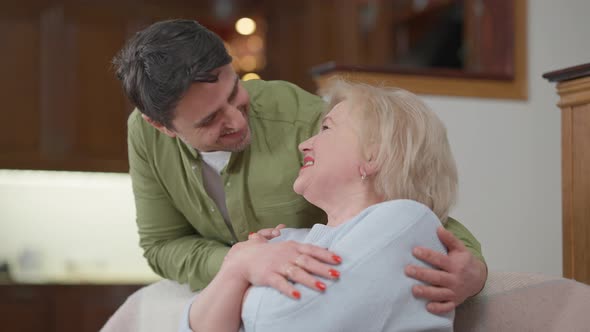 Cheerful Caucasian Senior Mother and Adult Son Hugging Looking at Camera Laughing