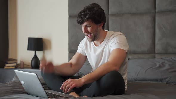 Excited Man Sitting on a Bed with a Laptop is Celebrating Success