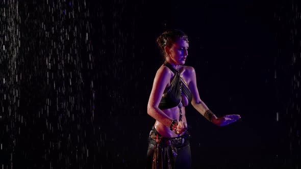 A Woman Dances an Oriental Dance on a Black Background in the Pouring Rain in the Studio