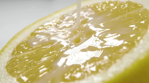 Fresh milk pours onto the bright surface of a half-ripe lemon in slow motion