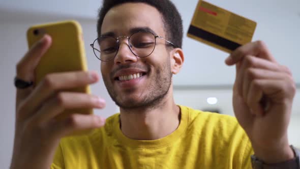 A Smiling Young AfricanAmerican Man with a Credit Card and a Smartphone