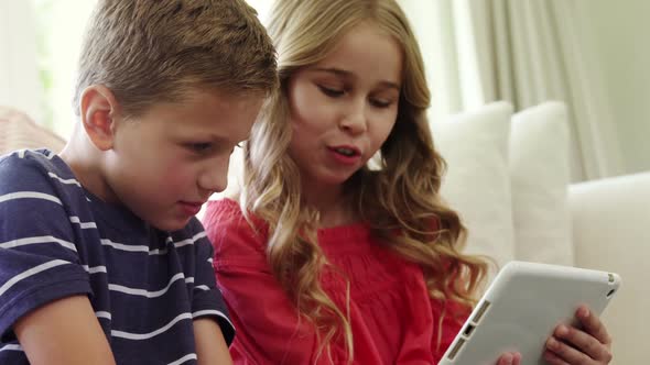 Siblings using digital tablet in living room