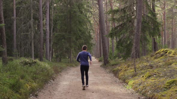 Brave lonely man walks and starts to run deep into forest on gravel road