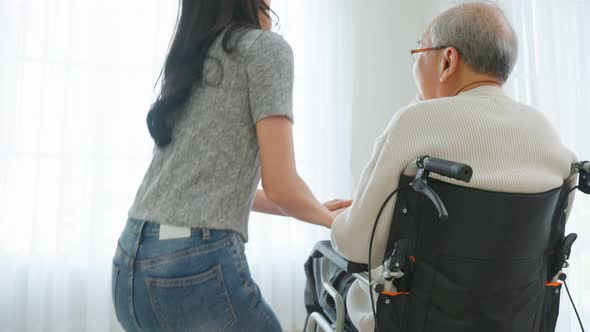 Asian young daughter take care senior male while sitting on wheelchair.