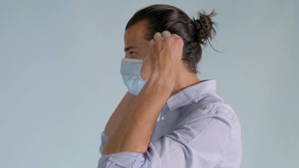 Left side shot of handsome man putting on hygienic mask. Static, bluish background