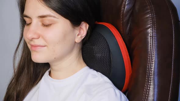 A Woman Sits in a Chair with a Massage Pillow and Does a Neck Massage