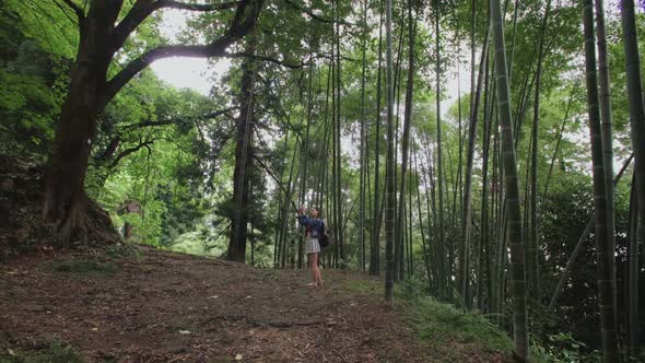 European Girl Traveler Takes Photo on Smartphone in Tropical Forest Trees Bamboo Plantation