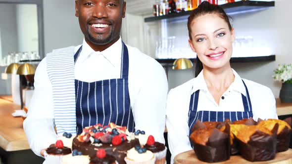 Portrait of smiling waiter and waitress presenting desserts at counter