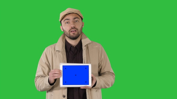 Man in trench walking and holding tablet with blue screen