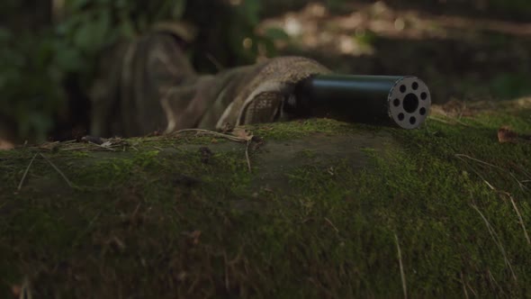 Closeup of Sniper Putting Out Rifle Muzzle with Suppressor on Log