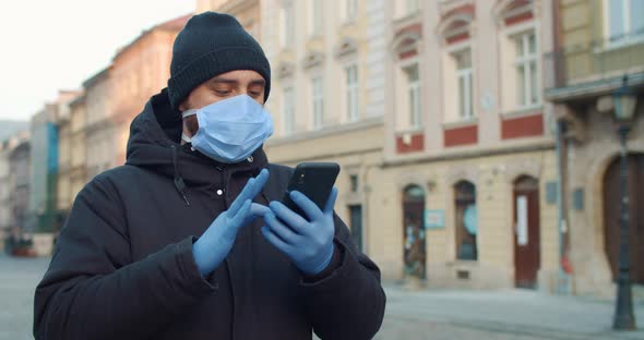 Man Scrolling News Feed and Looking at Phone Screen While Walking on Empty Street. Guy in Medical