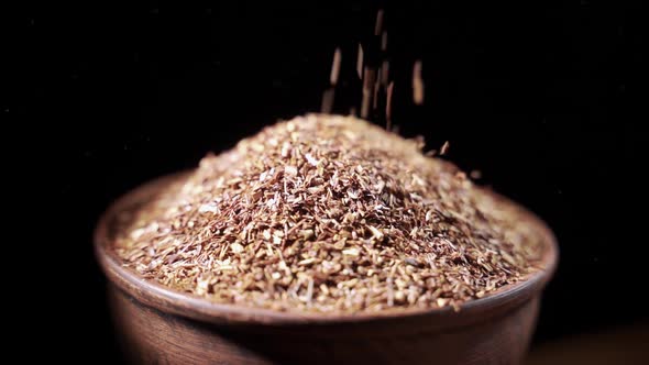 Flax Seeds are Poured Into an Earthenware Dish Closeup on a Black Background