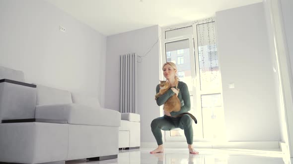 young fitness woman in sportswear performs squat exercises together with her pet in one at home 