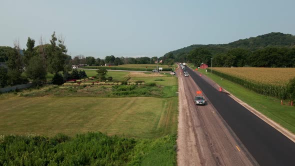 Drone view over rural highway being repaired with new asphalt. Lush green farm field. Blue sky. alt