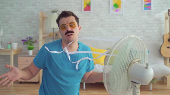 Funny Young Man in Front of a Working Electric Fan Escapes From the Heat in the Apartment