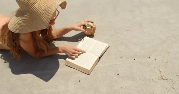 High angle view of Caucasian woman in hat reading a book on the beach 4k