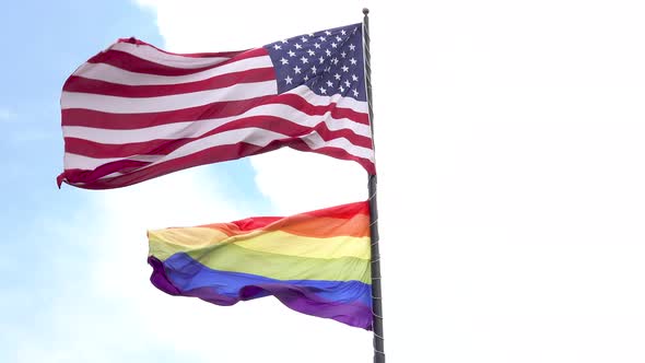 American flag and the rainbow LGBT pride gay pride flag waving in the wind with blue sky and clouds