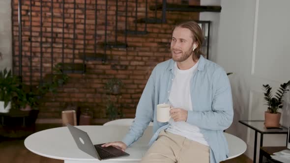 Busy Businessman in His Office Leading Conversation with Earplugs on and Drinking His Morning Office