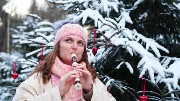 A woman plays a musical instrument at a Christmas tree in a winter snow-covered forest