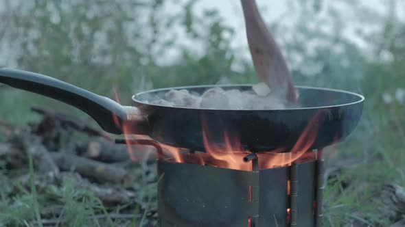 Person Frieing Meat in a Frying Pan on an Open Fire During a Picnic in the Forest