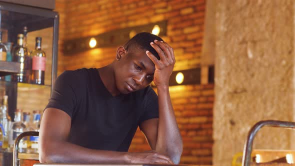 depressed black guy sitting in the pub holding his head with his hand