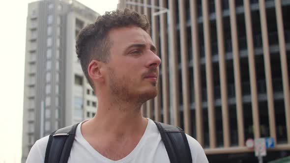 Portrait of a Young Handsome Man with a Backpack on the Background of Buildings in a Big City at