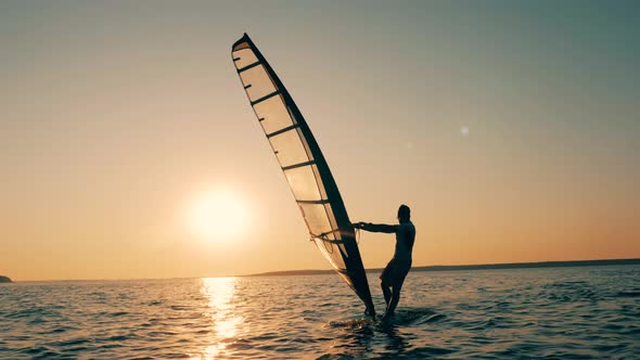 A Man Is Navigating a Windsurf Board During Sunset