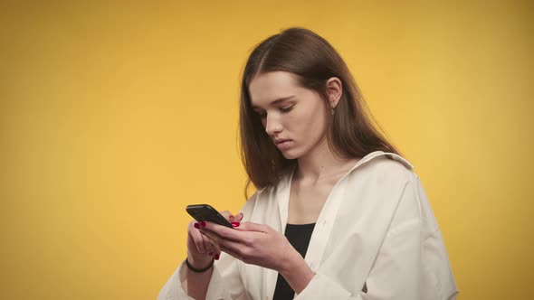 Young Adult Caucasian Woman is Surprised By a Deal on Her Smartphone on a Bright Yellow Background