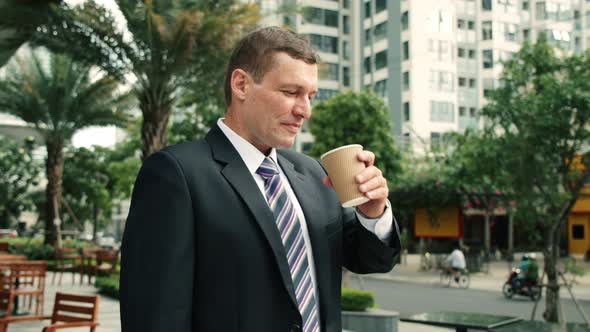 The Shot Moves Around a Businessman Standing on Street in the City Center Who and Drinks Hot