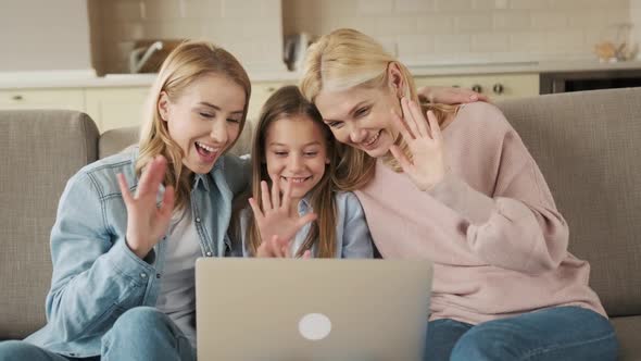 Happy Little Girl with Mother and Grandmother Using Laptop Together Sitting on Couch Looking at