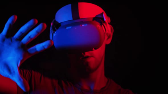 Young Man Plays a Game in a VR Helmet Under RedBlue Light