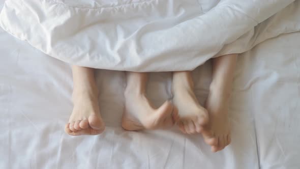 Two Pair of Feet Next To Each Other in a Bed. Mother and Daughter Lie on Bed with White Sheets.