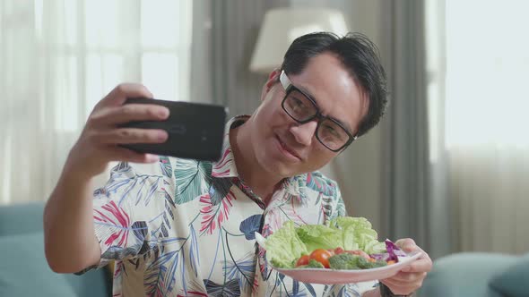 Close Up Of Smiling Asian Man Holding A Dish Of Healthy Food And Taking Selfie With Smartphone