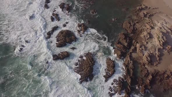 Foaming white ocean waves break over jagged rocks near shore, Buffalo Bay South Africa, aerial