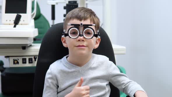 Little Boy in a Trial Frame for a Selection of Lenses is Sitting in an Optics Store