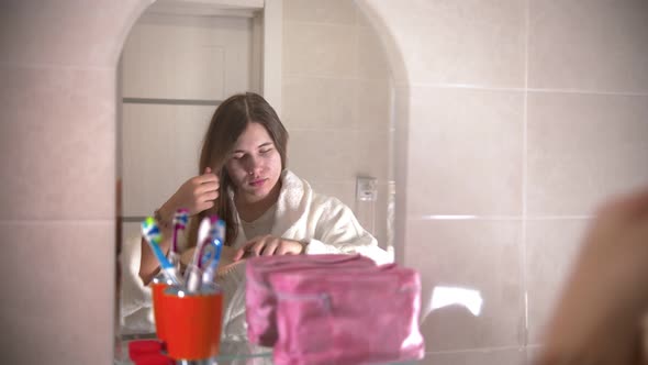 A Young Woman Brushes Her Hair Looking in the Mirror